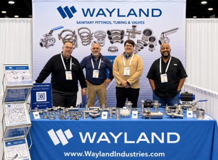 Four Wayland Industries team members at the PACK EXPO International 2026 booth in Chicago with sanitary fittings and valves on display.
